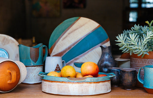 An assortment of blue, white and terracotta pottery on a wooden table. The pottery is made by Osa Atoe.